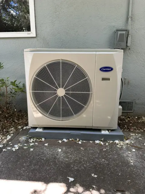 Carrier side-discharge heat pump on a raised pad beside a stucco wall in Concord