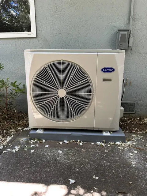 Carrier side-discharge heat pump on a raised pad beside a stucco wall in Concord